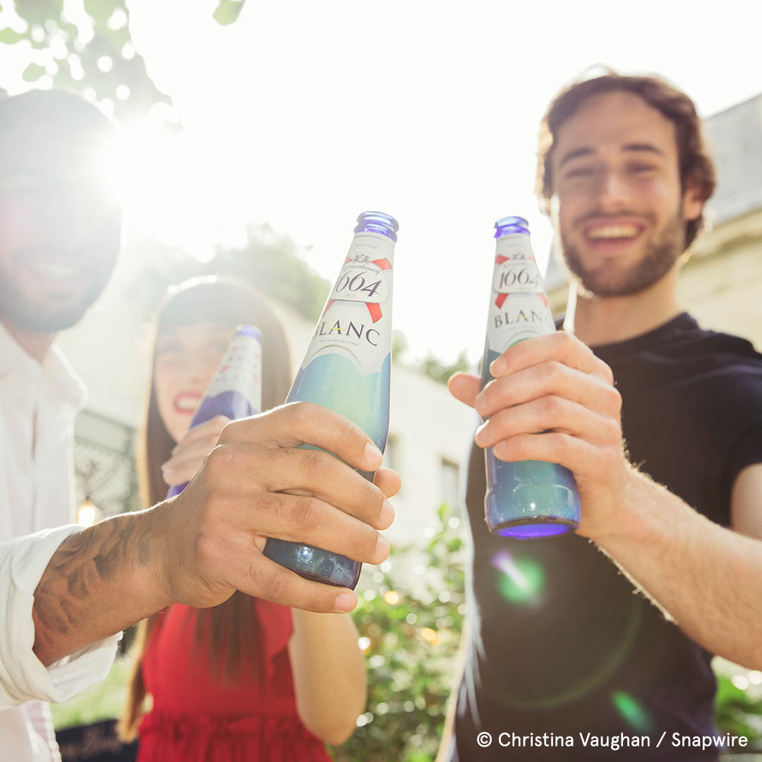 two people cheers bottles with the sun behind them