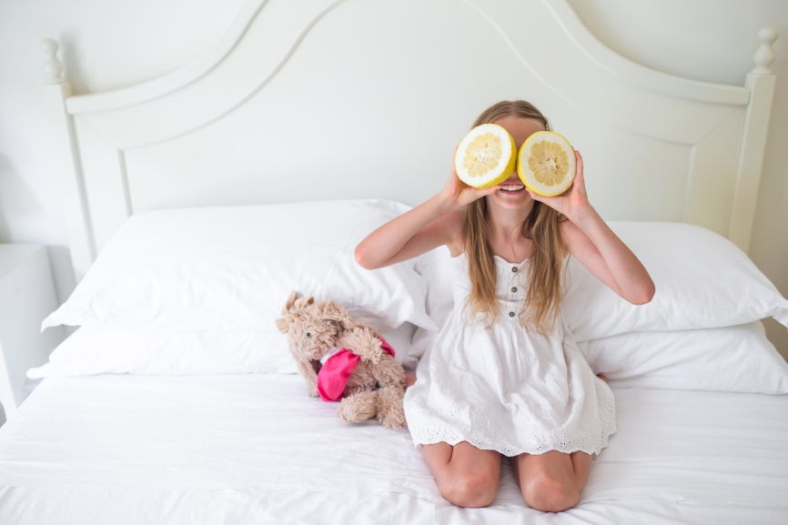 Little girl covering eyes with citrus lemons posing in her room
